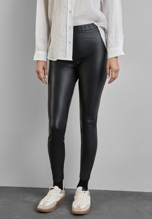 Zwarte faux leren leggings met een gladde textuur, hoge elastische tailleband, aansluitend ontwerp, gecombineerd met een witte blouse met knopen en sneakers.