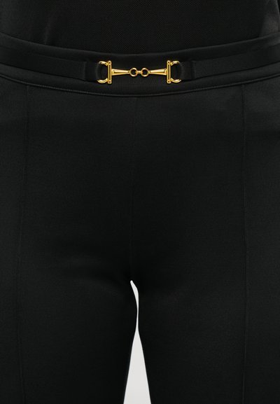 Pantalons noirs taille haute avec des détails de couture et une fine ceinture noire avec une boucle en forme de mors en or à la taille.