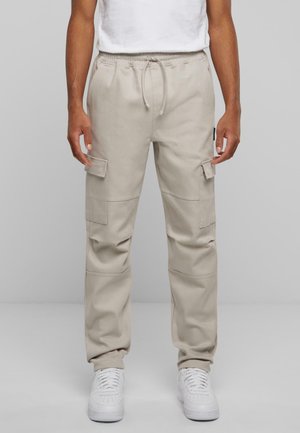 Pantaloni cargo bej cu talie elastică, șnur ajustabil, două buzunare laterale și picioare conice. Asortați cu adidași albi.