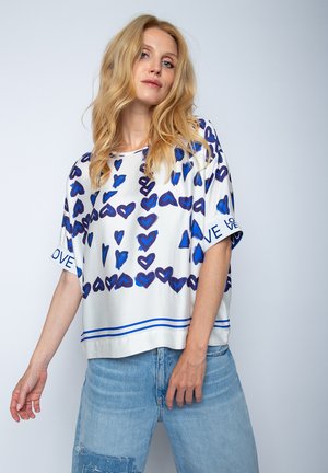 Kurzärmlige Bluse aus weißem Stoff mit blauen Herzmustern. Verfügt über einen runden Halsausschnitt und einen blauen gestreiften Saum.