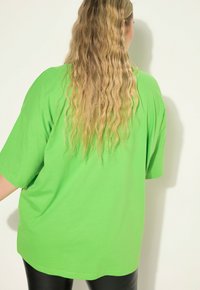 Camiseta de gran tamaño de color verde brillante, de manga corta, fabricada en material de algodón suave, de forma cuadrada, con detalles de costura mínimos, combinada con leggings negros.