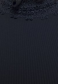 Černá látka s vertikálním žebrováním a jemnou krajkovou detailem na výstřihu. Textura se zdá být hladká a konzistentní po celém povrchu.