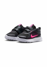 Zapatillas para niños pequeñas en negro y rosa con tela de malla, correas de velcro, suelas blancas y un logo de swoosh rosa de Nike en los lados.