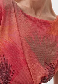 Tejido texturizado en rojo y naranja que presenta patrones abstractos en negro y gris, con un diseño drapeado y un amplio escote barco.