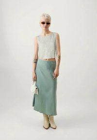 Ανοιχτό γκρίζο cropped top με υφή, σατέν φούστα σε μιντ πράσινο, μπεζ μπότες μέχρι το γόνατο και λευκή τσάντα. Το φόντο είναι απλό λευκό.