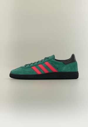 Zielony zamszowy sneaker Adidas z czerwonymi paskami, czarną podeszwą i piętą, z napisem "SPEZIAL" po boku.