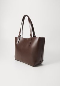 Sac fourre-tout en cuir brun au design structuré, texture lisse et détails en coutures verticales. Caractéristiques de longues anses plates pour un transport facile.