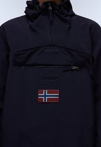 Marineblå vandtæt jakke med høj krave, frontlomme med lynlås og et rødt norsk flag-patch på brystet.