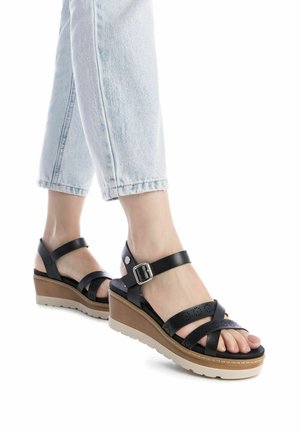 Sandali con tacco nero a forma di cuneo con più cinturini incrociati. Presentano un design perforato, chiusura con fibbia e una suola di colore chiaro per un contrasto.