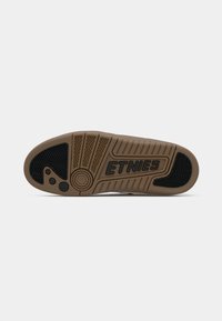Gumowa podeszwa w kolorze tan z czarnym akcentem. Wyposażona w teksturowany wzór, okrągły emblemat i wytłoczone logo "ETNIES" wyraźnie widoczne.