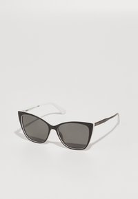 Occhiali da sole cat-eye bianco e nero con lenti scure, caratterizzati da un design affilato, finitura opaca e aste sottili di un bianco contrastante.