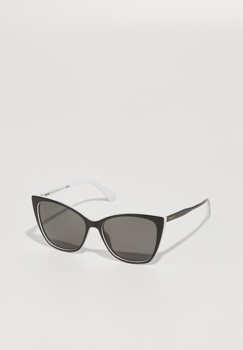 Occhiali da sole cat-eye bianco e nero con lenti scure, caratterizzati da un design affilato, finitura opaca e aste sottili di un bianco contrastante.