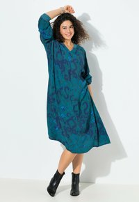 Vestido estampado en tonos azul verdoso y azul marino con escote en V y mangas tres cuartos. Diseño fluido, tela ligera, combinado con botas negras a los tobillos.