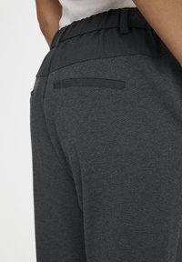 Mörkgrå träningsbyxor med elastisk midja och en enda bakficka, tillverkade av ett mjukt, texturerat tyg.