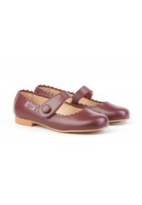 Zapatos Mary Jane de cuero burdeos con bordes festoneados, correa ajustable y suela plana de goma. Textura suave y diseño de punta redondeada.