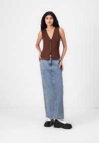 Top sans manches brun avec des boutons, associé à une jupe en denim longue bleu clair et des chaussures noires chunky. Tissu lisse et coupe décontractée.