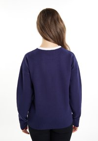Granatowy sweter z teksturowanej tkaniny, luźny krój i biały prążkowany kołnierz. Posiada długie rękawy i prążkowany dół.