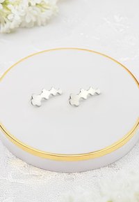 Silver blommiga örhängen med en polerad yta, som har tre sammanlänkade blad, visade på en vit cirkulär stång med en guldkant.