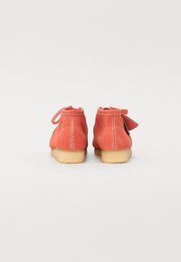 Botas de tobillo de ante coral con puntera redonda, cordones en la parte trasera y suela de goma ligera. Los detalles de costura añaden textura. Se muestra la vista trasera.