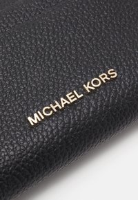 Black leather wallet with a textured surface, featuring a gold "MICHAEL KORS" logo. Compact design with visible stitching details.