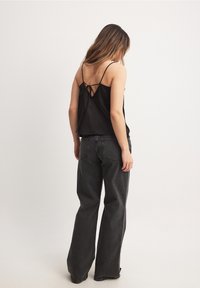 Camisole nera in satin con spalline sottili e dettaglio con lacci sul retro, abbinata a jeans scuri a vita alta, vista da dietro.