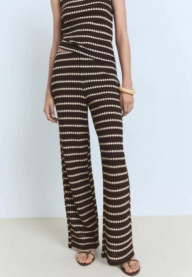 Combinaison en tricot rayée marron et crème avec un haut ajusté et un pantalon évasé. Texture lisse avec un motif en chevrons. Sandales plates portées.