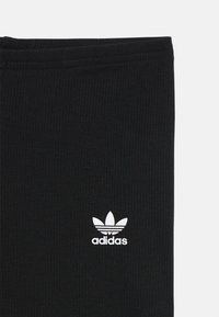 Fekete bordázott leggings, a bal alsó részen fehér Adidas logóval. Normál derékpánttal és sima textúrával rendelkezik.