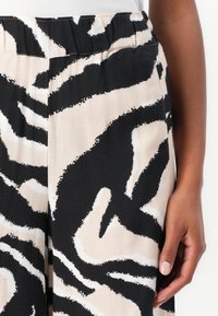 Pantalons abstraits noirs et blancs avec un fond beige ; tissu léger, taille élastique et design à jambes larges.