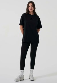 Svart oversized t-shirt med korta ärmar med en subtil logotyp, i kombination med svarta leggings och ljusa träningsskor.