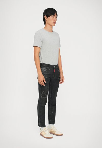 Camiseta gris de manga corta, jeans ajustados negros desgastados con pequeñas roturas y zapatillas blancas con acentos en beige. Diseño y ajuste sencillos.