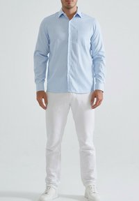 Chemise à rayures bleu clair avec des manches longues, un col et une poche poitrine, assortie à un pantalon blanc et des baskets blanches.