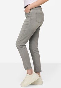 Jean de mezclilla gris con un corte ajustado, bolsillos frontales y un ligero recorte en el tobillo, combinados con zapatillas blancas con suela de plataforma.