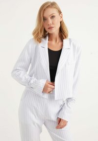 Korthytt vit kavaj med blå ränder, med notched krage och samlade ärmar. Bärs över en svart topp, som en del av en matchande kostym.