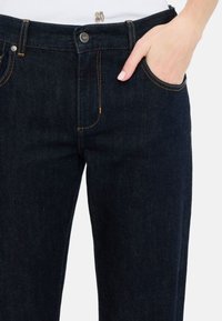 Jeans in denim scuro con un design classico a cinque tasche, cuciture arancioni e chiusura con bottone in vita, con una leggera elasticità.