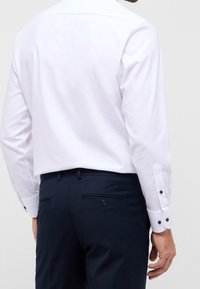 Camisa blanca de botones con cuello clásico, con botones de puño en color marino; combinada con pantalones marinos que tienen dos bolsillos traseros.