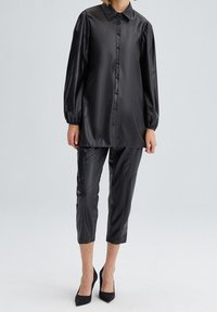 Svart syntetisk läder skjorta med knappar, axeldetaljer och långa puffärmar, tillsammans med matchande tapered cropped byxor och svarta klackar.