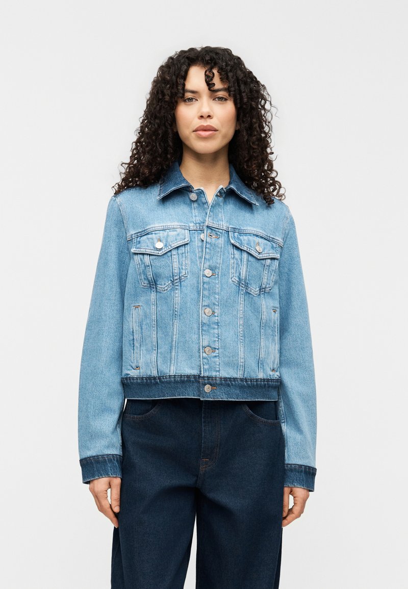 Ανοιχτό μπλε τζιν μπουφάν με κλείσιμο κουμπιών, δύο τσέπες στο στήθος και κοντή σχεδίαση. Διαθέτει κλασικό γιακά και αντίθετη ραφή.