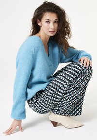 Lichtblauwe gebreide trui met V-hals; geprinte zwarte en blauwe driehoekige broek; witte enkelboots met hak, van gestructureerde stof.