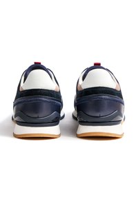 Marineblaue Sportschuhe aus Leder und Wildleder mit weißen Akzenten, rundem Absatz, rotem Laschenetikett und profilierter Gummisohle für besseren Halt. Ansicht von hinten.