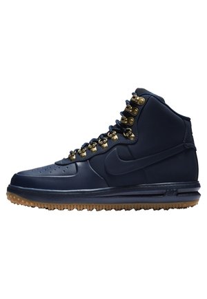 Basket montante bleu marine Nike avec œillets dorés, lacets bleu foncé, semelle en gomme et logo Nike swoosh en relief sur le côté.