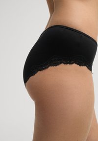 Culottes en coton noir avec une bordure en dentelle festonnée le long de l'ourlet, une texture lisse et une coupe ajustée.