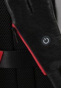 Guanto in pelle nera con una zip rossa e un'icona del simbolo di alimentazione. Lo sfondo in rete testurizzata aggiunge contrasto. Il design complessivo unisce funzionalità e stile.