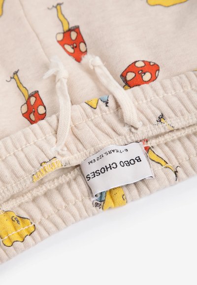 Tissu beige avec des imprimés colorés de champignons et de bananes, taille élastique avec cordons, et une étiquette de vêtement attachée.