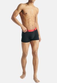 Μαύρα μποξεράκια με κόκκινη ελαστική μέση που έχει λογότυπο. Το ύφασμα φαίνεται λείο και εφαρμοστό, τονίζοντας το σχήμα και την άνεση.