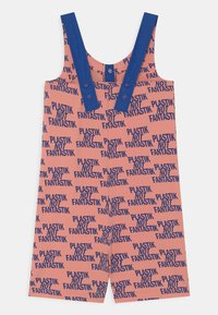 Macacão cor de rosa com alças ajustáveis azuis, apresentando um padrão repetido do texto "PLASTIK NOT FANTASTIK" em azul marinho. Textura de tecido suave.