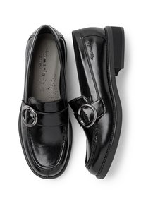 Paire de mocassins en cuir noir avec boucles rondes argentées et semelles épaisses, indiquée comme large et marquée "Tamaris" à l'intérieur et sur le côté.