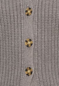 Siva pletena cardigan s tremi velikimi, okroglimi rjavimi in zlatimi gumbi na sredini, z teksturiranim, rebrastim materialom.