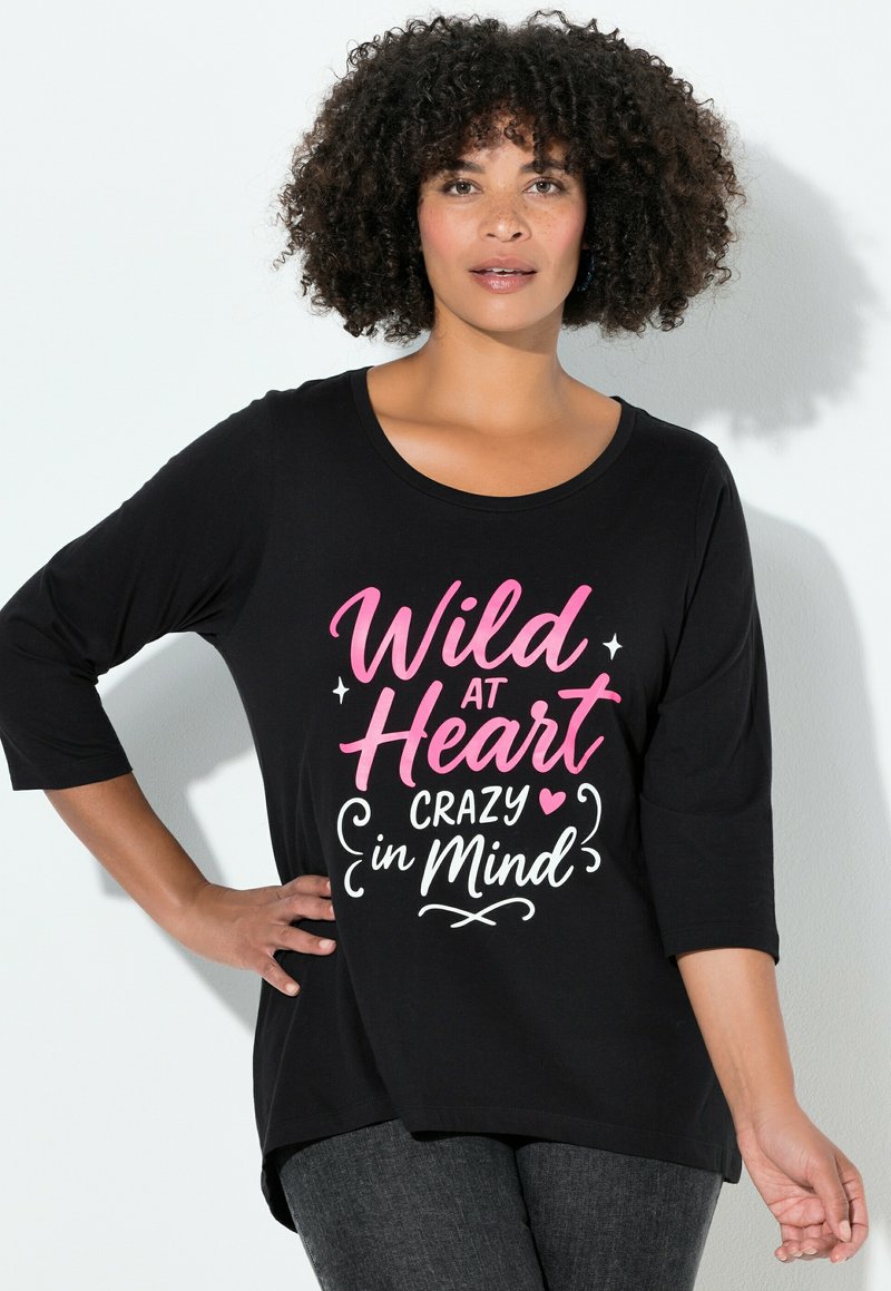 Černé tričko s rukávy do tří čtvrtin, s růžovým a bílým nápisem „Wild at Heart Crazy in Mind“ na hladké, elastické látce.