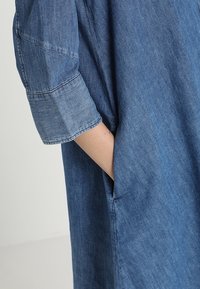 Jeansskjorta med upprullade ärmar, som har en avslappnad passform och sidofickor. Tyget är blått med en något strukturerad yta.