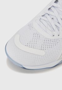 White athletic shoe featuring a mesh upper with textured detailing, a smooth rubber toe cap, and a semi-transparent blue sole.